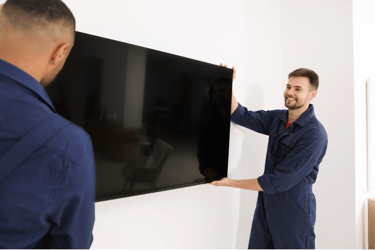 Zwei Handwerker montieren gemeinsam einen Fernseher an der Wand